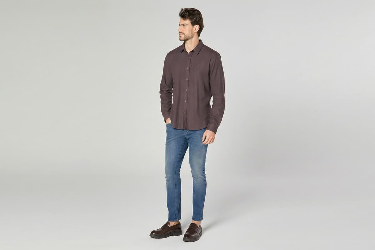 modelo usando sapato marrom calca jeans e camisa marrom em fundo cinza