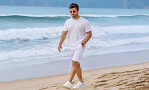 homem caminhando na praia com camiseta branca e bermuda clara